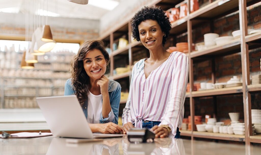 Duas empresárias em loja planejando crescimento da empresa e comparando opções de capital próprio e capital de terceiros para financiamento.