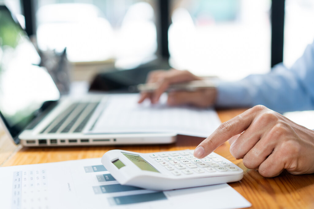 Pessoa no notebook e fazendo cálculos na calculadora para identificar o melhor cdb prefixado ou pos fixado