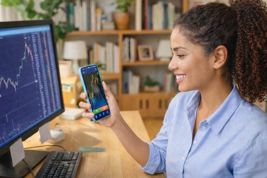 Mulher acompanhando gráficos de investimentos no celular em home office, analisando rendimento de CDB e CDI