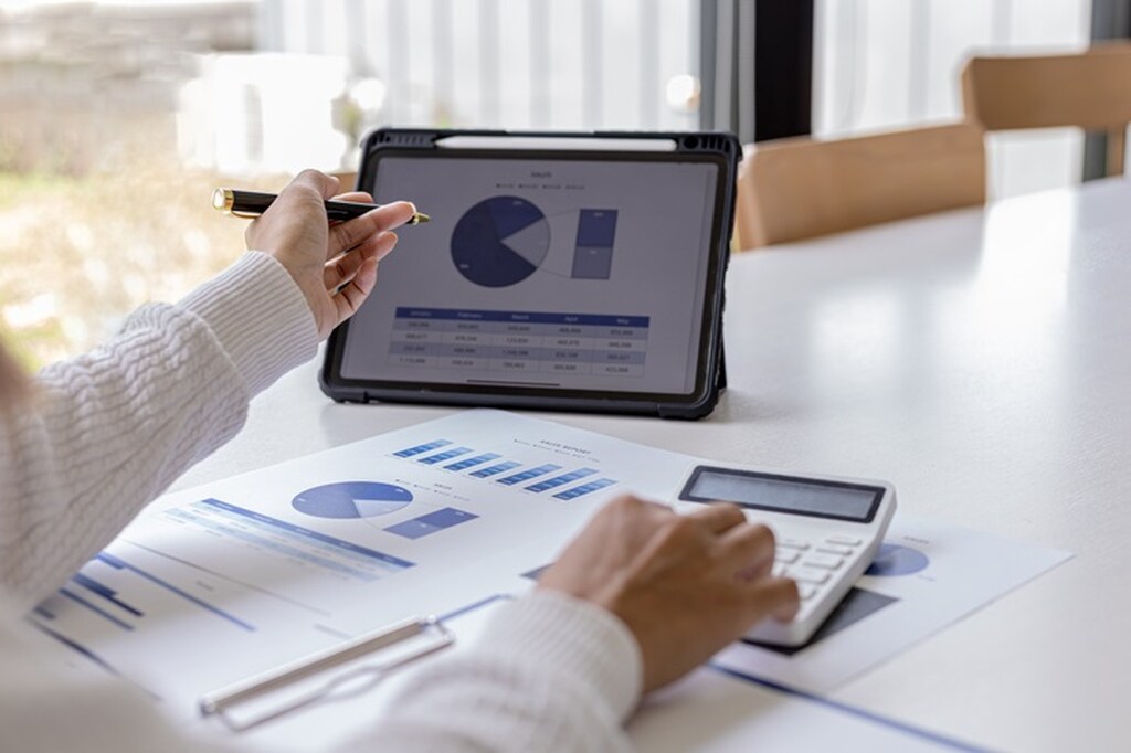 Pessoa analisando empresas que pagam dividendos mensais com tablet e gráficos.