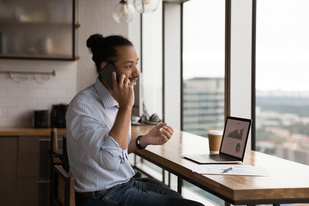 Investidor falando ao telefone e usando notebook para pesquisar os melhores investimentos de curto prazo.