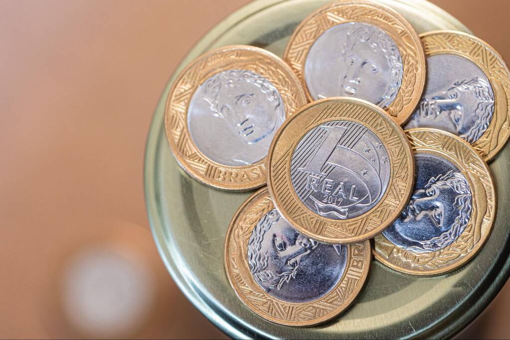 Moedas de um real representando investimentos e cálculos sobre quanto rende 100 mil no CDI por mês.