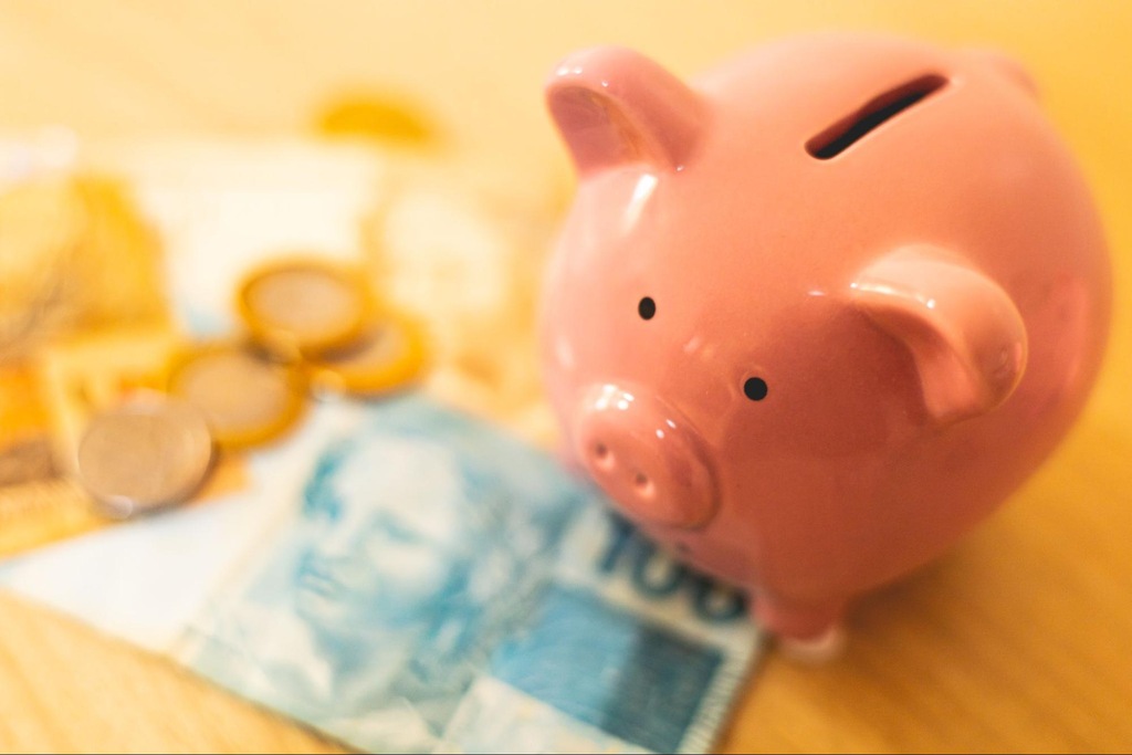 porquinho ao lado de moedas e nota de dinheiro representando quanto rende 100 mil no CDI por mês.