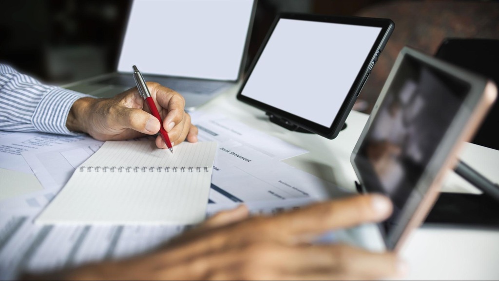 Pessoa analisando notas e registros financeiros em tablet e papel, etapa comum em operações de risco sacado.