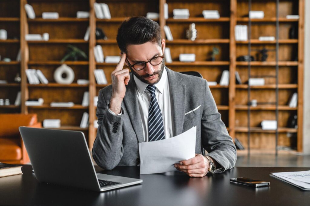 Homem em escritório segurando papel e com a mão direita na têmpora, analisando diferenças entre CDB e fundo de investimento.