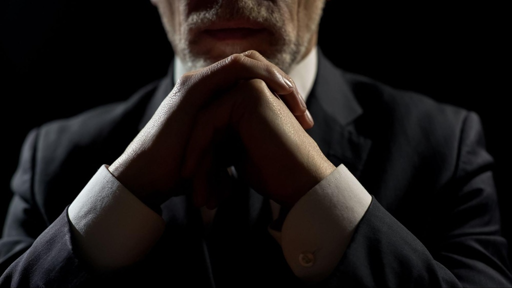 Parte do rosto de investidor usando terno, com as mãos juntas em frente ao queixo, avaliando se vale mais a pena investir em CDB ou LCI.