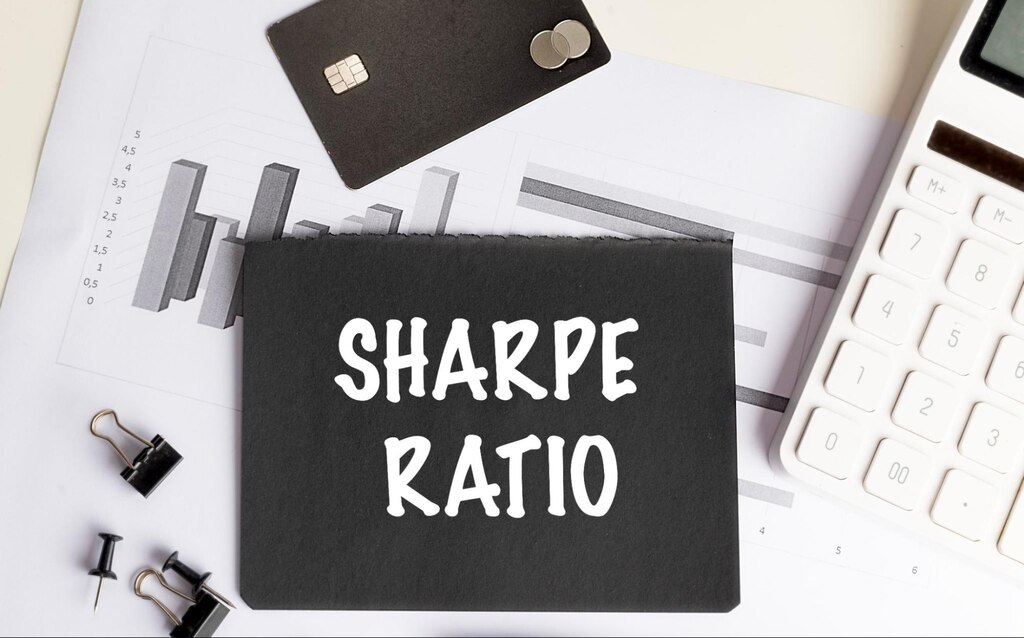 Mesa de escritório com papeis, cartão e calculadora. Na frente, uma nota com fundo preto com as palavras "Sharpe Ratio" escritas em branco.