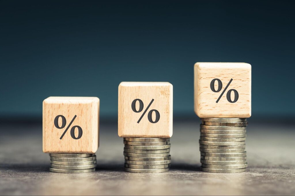 Dados de % em cima de pilhas de moedas em ordem crescente, representando juros futuros.