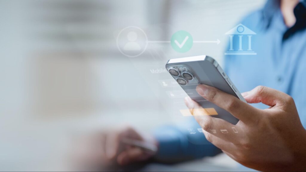 Detalhe de mão de pessoa segurando smartphone, pesquisando melhor banco para investir em fundos imobiliários, enquanto ícones digitais representando bancos e negociações financeiras circulam o aparelho.