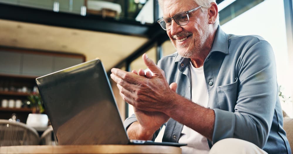 Homem sorrindo enquanto usa notebook em ambiente acolhedor, representando a satisfação ao investir por meio de um banco de investimento.