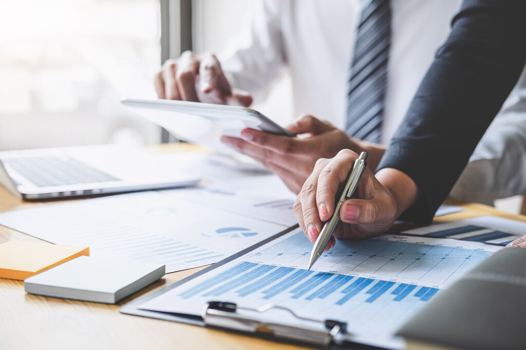 Duas pessoas em escritório financeiro, utilizando gráficos para entender como o Imposto de Renda afeta o CDB.