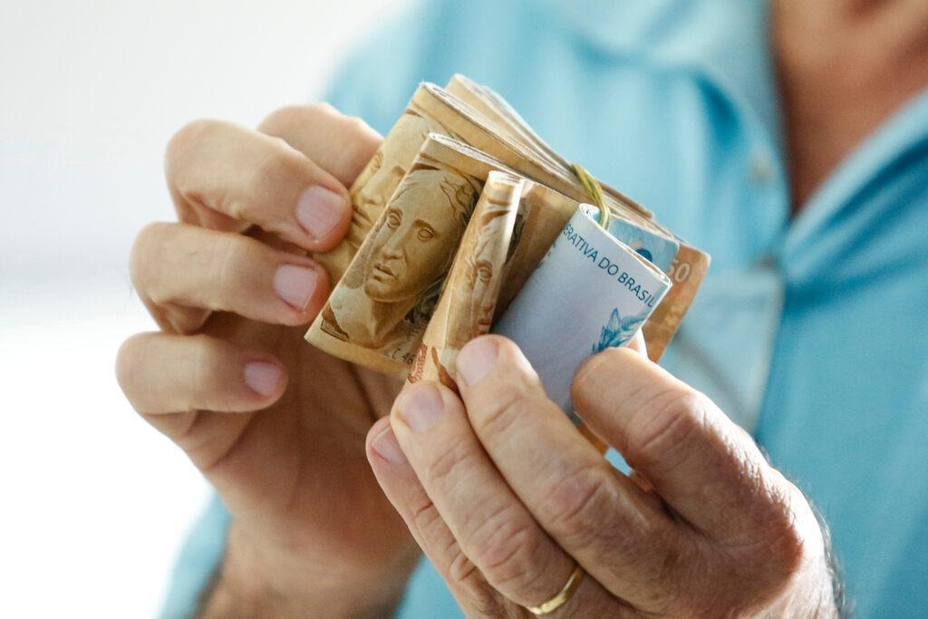 Pessoa segurando diversos maços de notas de reais, simbolizando 20 mil para investir.