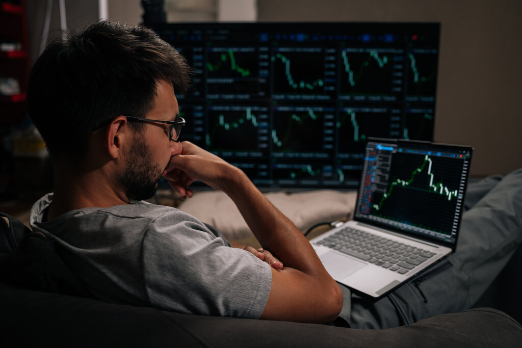 Homem utilizando monitores com dados financeiros para começar a investir.