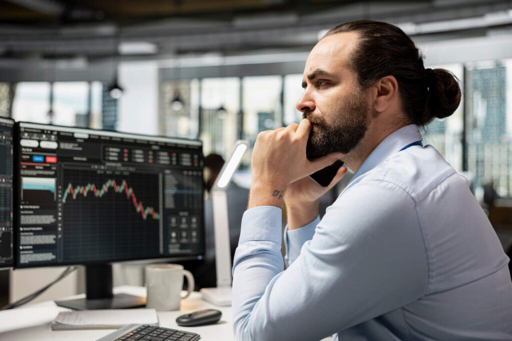 Homem analisando gráficos de ações no computador em ambiente de escritório, representando estratégia de swing trade no mercado financeiro.